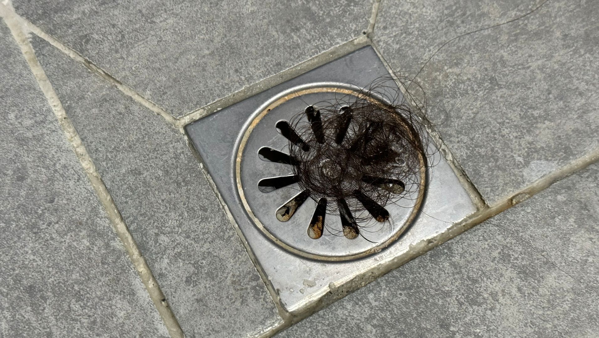 A clogged floor drain surrounded by debris such as hair, soap residue, and small objects.