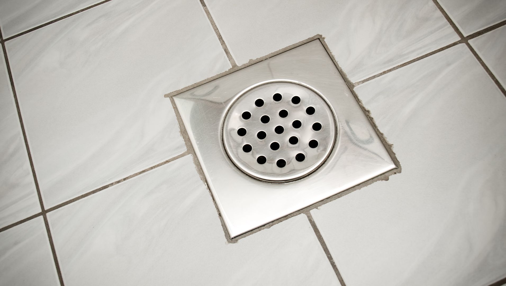 A person cleaning a floor drain with a brush and hot water